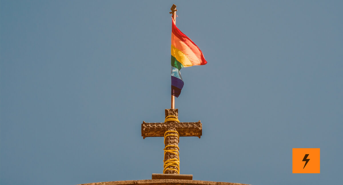 Auf dem Kreuz einer Kirche steht eine LGBTQ+ Flagge.