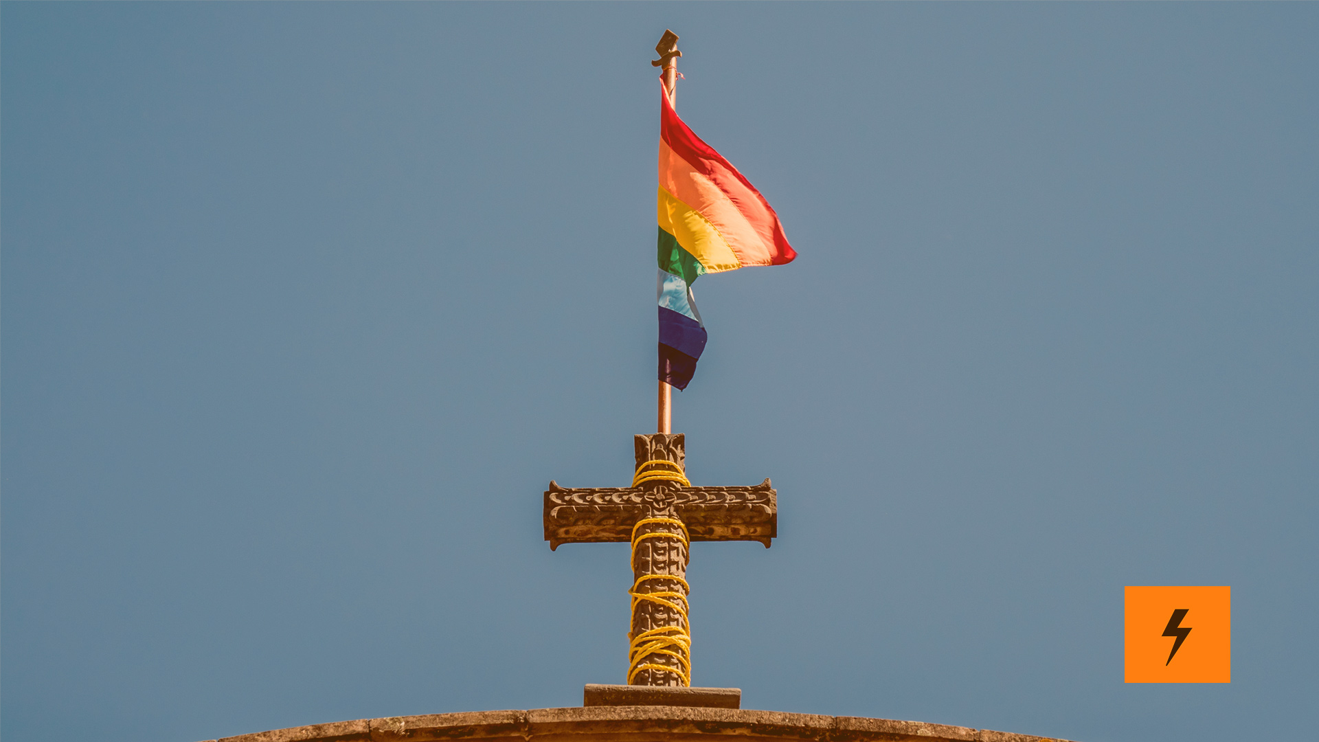 Auf dem Kreuz einer Kirche steht eine LGBTQ+ Flagge.