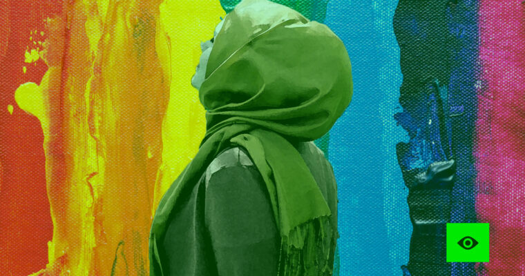 Eine Frau mit Kopftuch schaut zu einer Wand, die in den LGBTQ+ Farben angemalt ist.