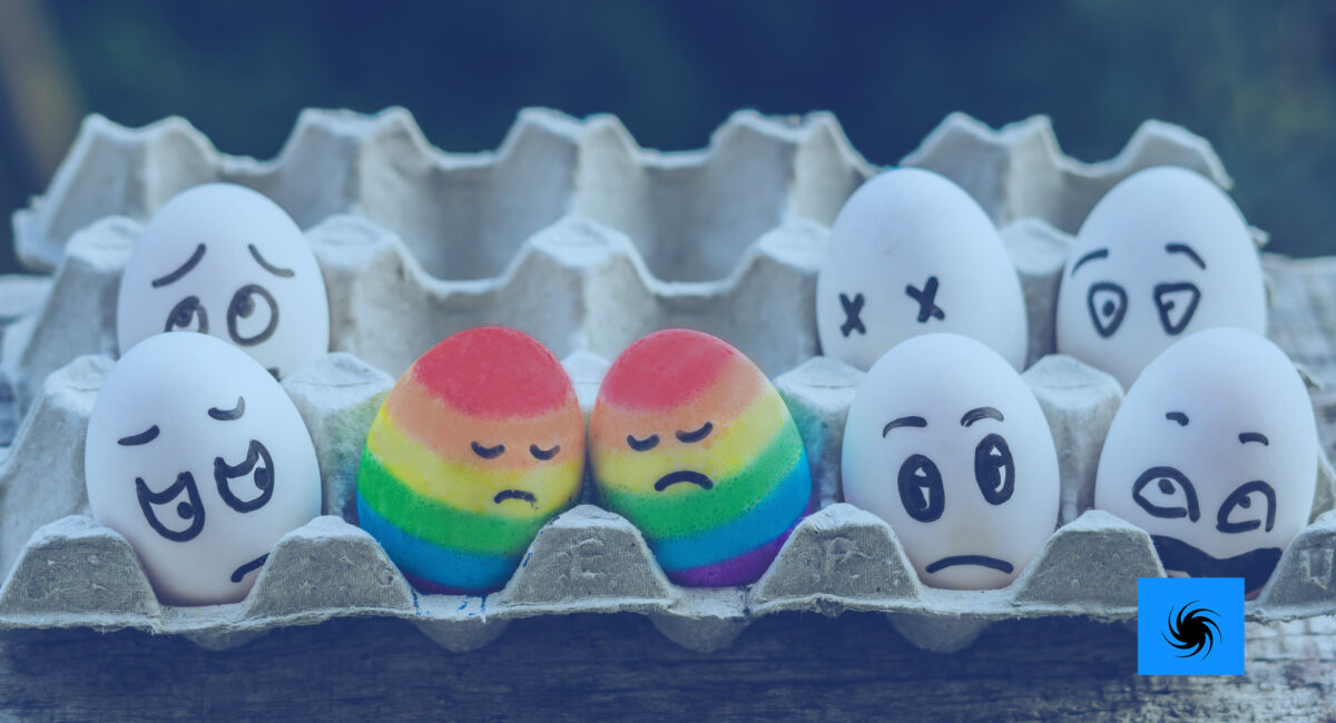 In einem Eierkarton sind zwei Eier in den LGBTQ+ Farben eingefärbt und werden von den andere Eiern komisch angeschaut.