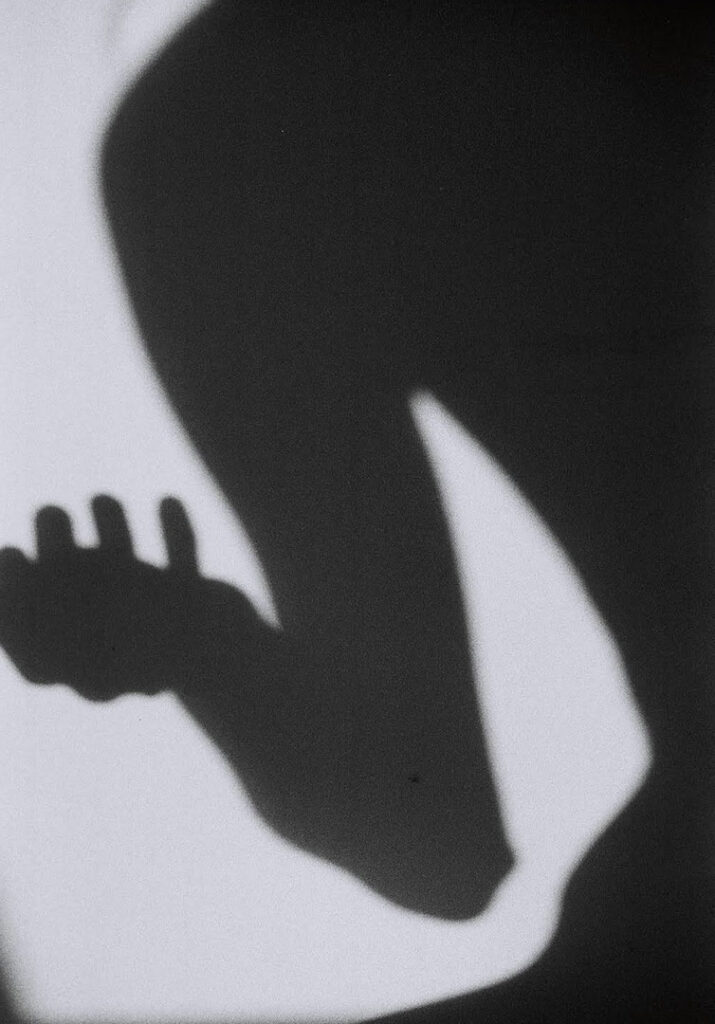 Schatten einer Gestalt gegen die Wand. Die Hand ist offen.