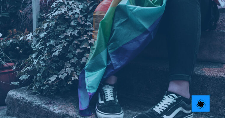 Eine Person sitzt mit einer Pride Flagge auf einer Treppe: Man sieht nur die Beine.