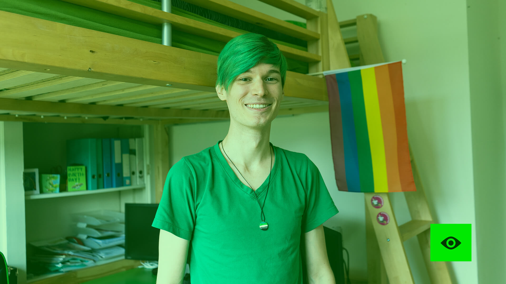 Janis steht in seinem Zimmer, vor dem Hochbett, wo die Pride-Flagge hängt.